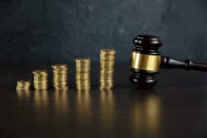 Close-up Of A Judge's Hand Holding Gavel Over Stacked Golden Coins